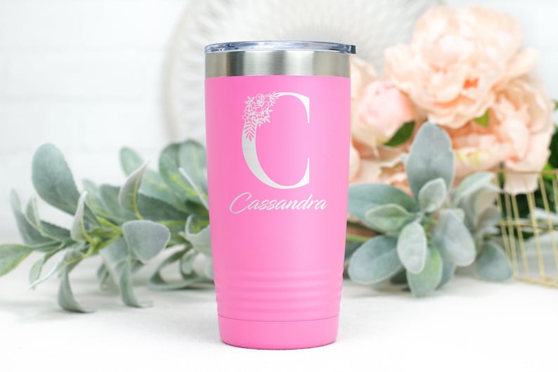 K&ouml;nnte beinhalten: Rosafarbener Edelstahlbecher mit einem wei&szlig;en Blumenmuster und dem Buchstaben "C" sowie dem Namen "Cassandra" auf der Vorderseite.