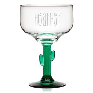 May include: A clear glass margarita glass with a green cactus stem and base. The glass is engraved with the name "Heather".