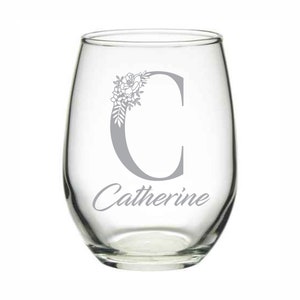 Puede incluir: Una copa de vino sin tallo de vidrio transparente con un dise&ntilde;o floral gris y la letra "C" y el nombre "Catherine" grabados en la parte delantera.