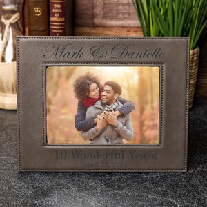 May include: A brown leather picture frame with a stitched border. The frame has a photo of a couple smiling and hugging. The frame is engraved with the text "Mark & Danielle" and "10 Wonderful Years April 22, 2014".