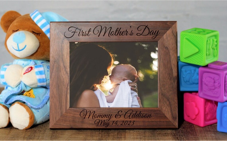 Pu&ograve; includere: Una cornice per foto in legno marrone con una foto di una madre e un bambino. La cornice &egrave; incisa con il testo "First Mother's Day" e "Mommy & Addison May 14, 2023".