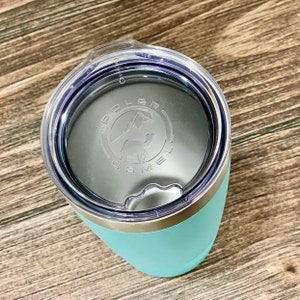 May include: A turquoise travel mug with a silver lid and a clear plastic lid with a silver band. The clear lid has a logo that says "Dolce Brew Co."