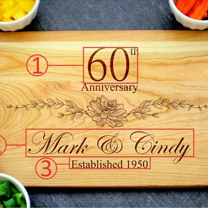 K&ouml;nnte beinhalten: Ein Holzbrett zum Schneiden mit einem Blumendesign und dem Text "60. Jahrestag", "Mark & Cindy" und "Gegr&uuml;ndet 1950".