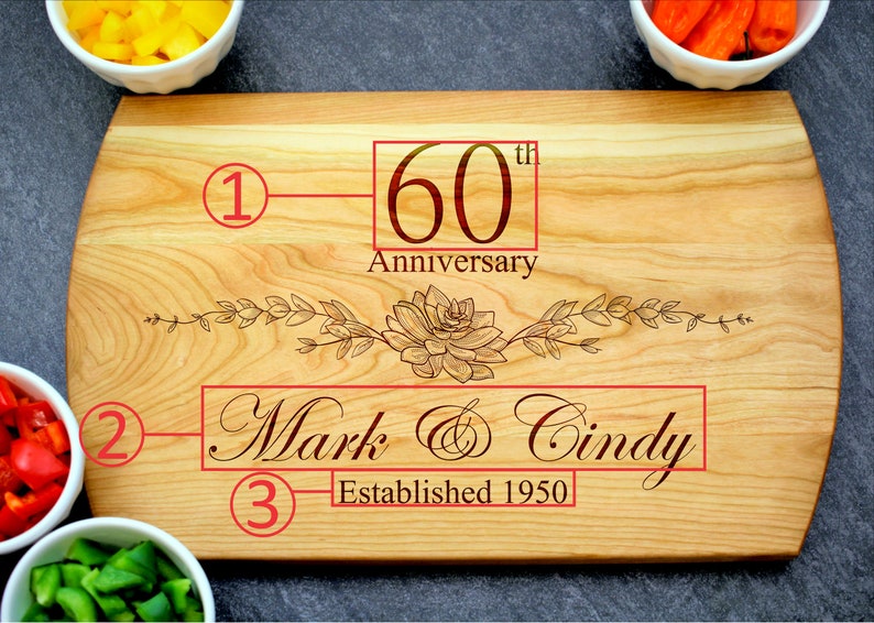 K&ouml;nnte beinhalten: Ein Holzbrett zum Schneiden mit einem Blumendesign und dem Text "60. Jahrestag", "Mark & Cindy" und "Gegr&uuml;ndet 1950".