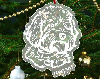 May include: A clear acrylic Christmas ornament featuring a white silhouette of a dog with the name "Nugget" written below. The ornament is hanging on a Christmas tree.