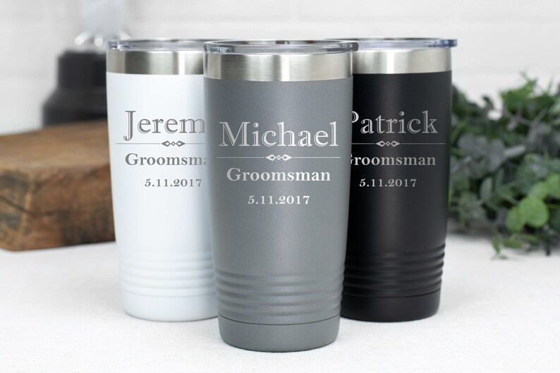 May include: Three stainless steel tumblers with personalised engravings. The tumblers are in white, grey, and black. The engravings include the names "Jerem", "Michael", and "Patrick", the word "Groomsman", and the date "5.11.2017".