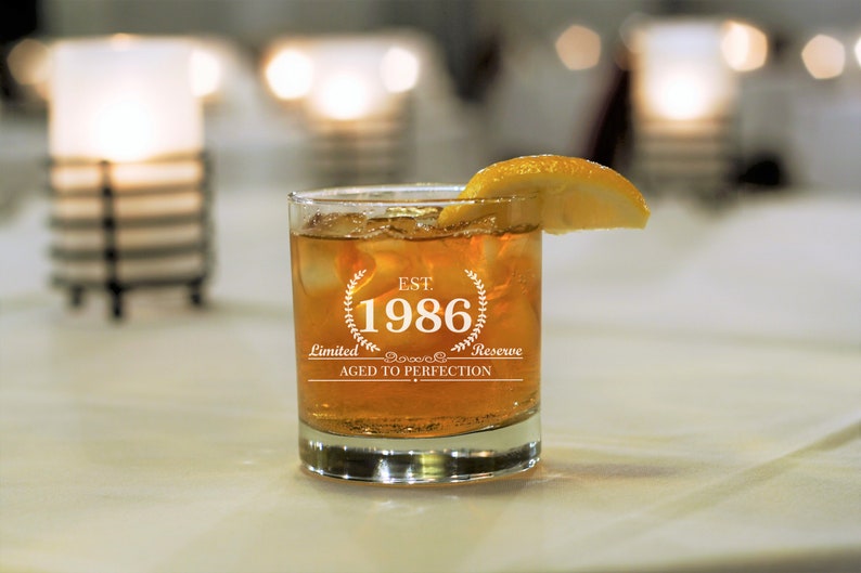 May include: A clear glass with ice and a lemon wedge. The glass has the text "EST. 1986 Limited Reserve Aged to Perfection" etched on the side.