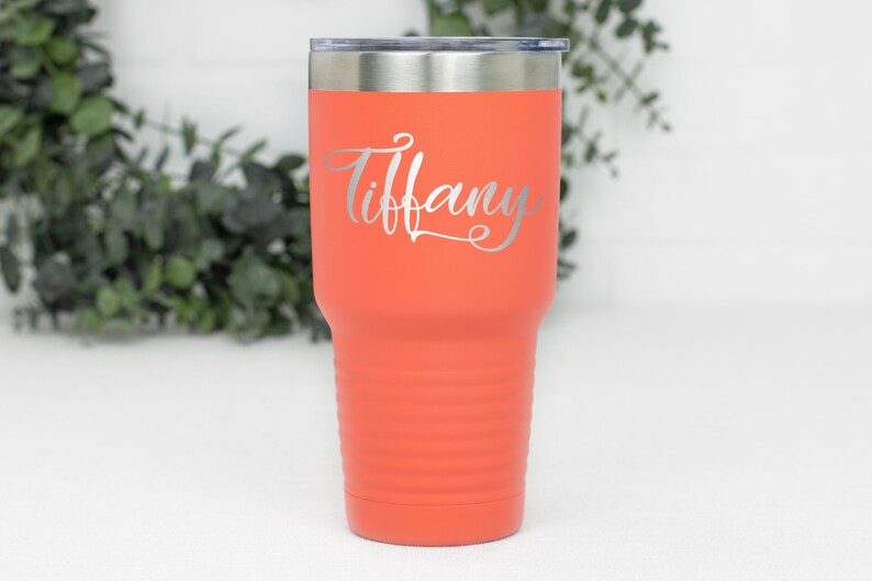 Puede incluir: Un vaso de acero inoxidable de color coral con una tapa plateada y el nombre "Tiffany" grabado en el lateral.