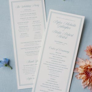 以下が含まれることがあります： 薄い青色の縁とテキストが入った2つの結婚式のプログラム。プログラムには、結婚式のパーティー、式の順序、名前が記載されています。フローラルのアクセントが散らばっています。