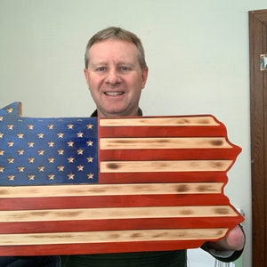 May include: A wooden sign in the shape of Pennsylvania, featuring the American flag design. The blue section has gold stars, and the red and white stripes are visible. The sign is made of wood and has a rustic, distressed look.