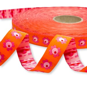 Könnte beinhalten: Eine Rolle orangefarbenes Band mit aufgedruckten rosa Blumen. Das Band ist gerollt und die Rolle ist im Hintergrund sichtbar.