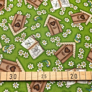 Könnte beinhalten: Grüner Stoff mit einem sich wiederholenden Muster aus braunen Vogelhäusern mit Herzen, weißen Blumen und blauen Vögeln. Ein Holzlineal mit Markierungen in Zentimetern befindet sich am unteren Rand des Bildes.