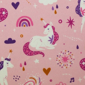 Könnte beinhalten: Rosafarbener Stoff mit einem sich wiederholenden Muster aus Einhörnern, Regenbögen, Sternen, Herzen und Wolken. Die Einhörner sind weiß mit rosa und violetten Mähnen und Schwänzen.