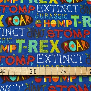 Könnte beinhalten: Blauer Stoff mit einem sich wiederholenden Muster aus bunten Dinosaurier-Wörtern wie "T-Rex", "Roar", "Stomp" und "Extinct".