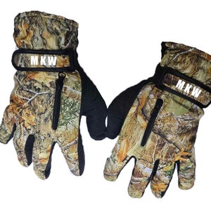 May include: A pair of brown and green camouflage gloves with black accents and a zip on the back of each glove. The gloves have a black strap with the text "MKW" in white letters.