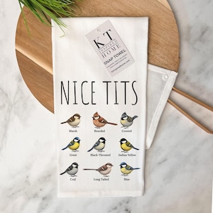 Peut inclure: Un torchon de cuisine blanc avec le texte "NICE TITS" en lettres noires au-dessus de neuf illustrations de différentes espèces d'oiseaux, chacune étiquetée avec son nom : Marsh, Bearded, Crested, Great, Black-Throated, Indian Yellow, Coal, Long Tailed et Blue.