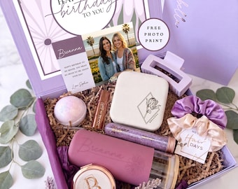 May include: A lavender gift box containing a personalized tumbler with a daisy design, a white jewelry case with a floral graphic, a round compact mirror with a letter B, a purple hair claw, a satin scrunchie, a bath bomb, and a photo print.