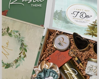 May include: A gift box containing a gold tumbler, a compact mirror with the letter R, heart-shaped sunglasses, a brown notebook, a bottle stopper, a candle labeled You're So Fire, a bath bomb, and two scrunchies. The box lid features a floral wreath.