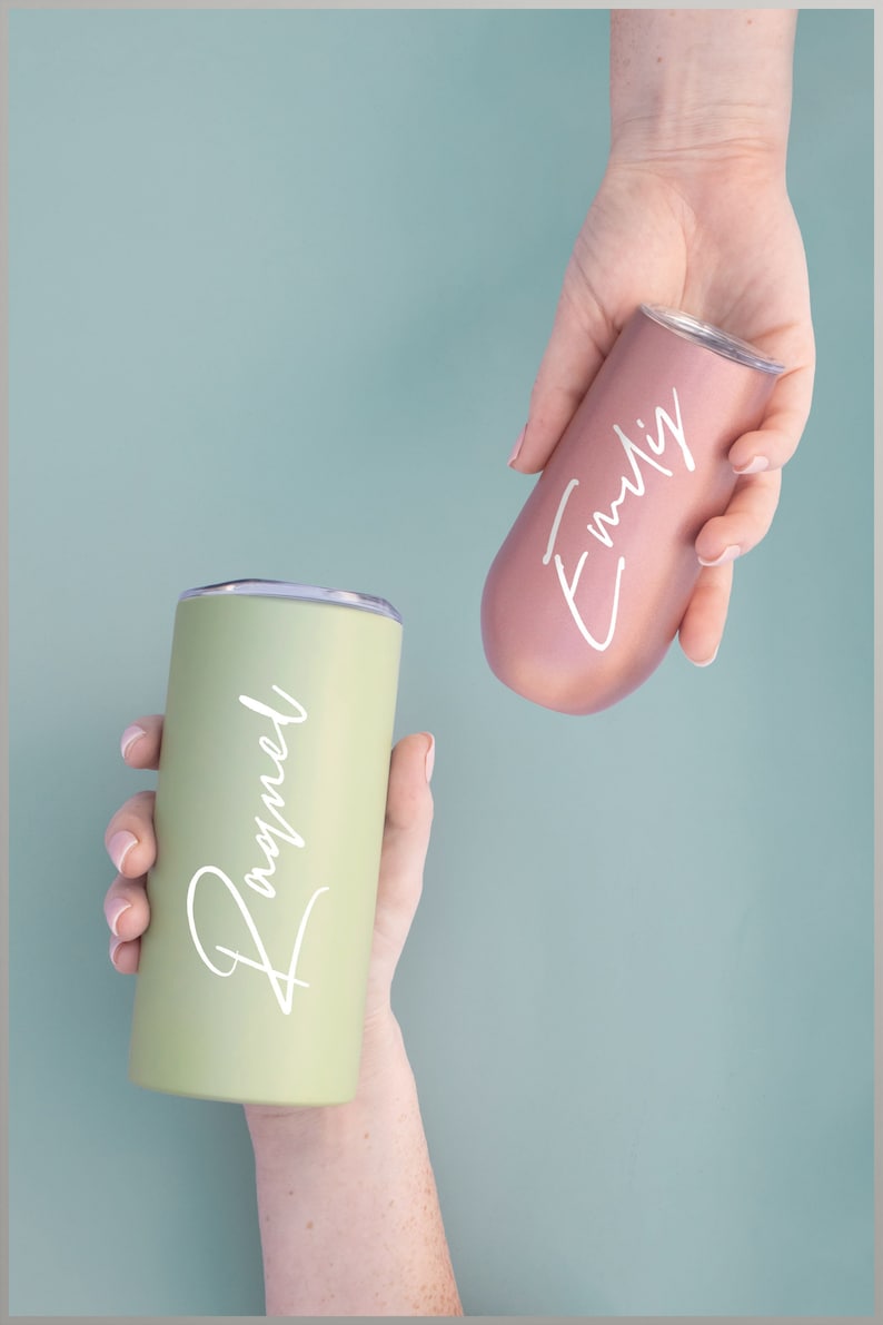 May include: Two insulated tumblers, one sage green and one rose gold, are held in hands. Each tumbler has a white script name: "Raquel" on the green tumbler and "Emily" on the rose gold tumbler. The background is a solid, muted teal.