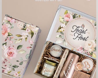 May include: A spa gift hostess gift set in a floral box containing a bath bomb labeled Soak, a candle labeled Glow, a tube of bath salt, a rose gold tumbler personalized with the name Brianna, a compact mirror with a B, and a bar of soap labeled Wash.