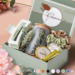 May include: A gift box with a variety of items, including a white hair clip, a tumbler with gold text, a compact mirror, and scrunchies. The box lid has the text "Will you be my bridesmaid?" and a floral design. The box is light green.