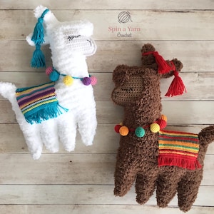 May include: Two handmade crochet llama dolls. One is white with blue tassels and a colorful blanket, the other is brown with red tassels and a colorful blanket. Both have closed eyes and a pom-pom necklace. The text "Spin a Yarn Crochet" is in the upper right corner.