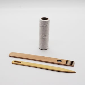 Puede incluir: Un conjunto de herramientas de tejido que incluye una bobina de hilo blanco, una aguja de madera con un agujero y un peine de madera con cuatro dientes.