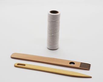 May include: A set of weaving tools including a spool of white yarn, a wooden needle with a hole and a wooden comb with four teeth.