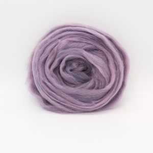 Puede incluir: Primer plano de una bola de vellón de lana de color lavanda. La lana es suave y esponjosa, y es perfecta para hilar o fieltro.