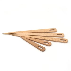 May include: Set of five wooden knitting needles with a pointed tip and a small hole at the end. The needles are arranged in a fan shape on a white background.