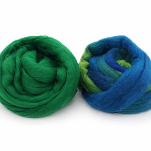 May include: Two balls of wool roving. One is a solid, vibrant green. The other is a blend of blues and greens. The wool is soft and fluffy, ideal for fiber art projects like needle felting or spinning.