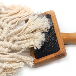 May include: A close-up of a wooden brush with black bristles and a wooden handle. The brush is covered in white fibers, likely from a piece of fabric.