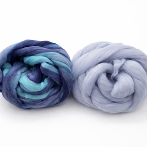 May include: Two bundles of wool roving. One is a blend of blues and teals, the other is a solid light blue. The wool is tightly coiled, showing the texture of the fibers. Ideal for fiber art projects.