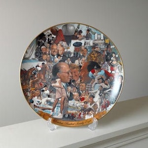 Peut inclure: Une assiette en céramique blanche avec un bord doré présente un collage coloré d'images et de texte. L'assiette représente un groupe de personnes, dont un homme en costume et une femme en robe. Le texte sur l'assiette indique "National Baseball Society 1993".