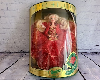 May include: A red and gold Barbie doll in a red gown with a green and red poinsettia. The doll is in a clear plastic box with a gold trim and the words "Happy Holidays" and "Special Edition" on the box. The box also has the Barbie logo.