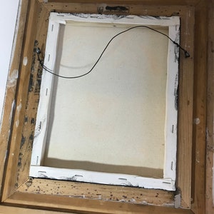 May include: The back of a framed canvas painting with a white canvas and a wooden frame. The frame is a light brown color and has a few dark brown spots on it. There is a black wire attached to the back of the canvas.