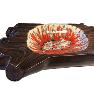 May include: A ceramic ashtray with a distinctive design. It's shaped like a piece of wood, with a central bowl displaying a red and white floral pattern. The exterior is a dark brown colour.