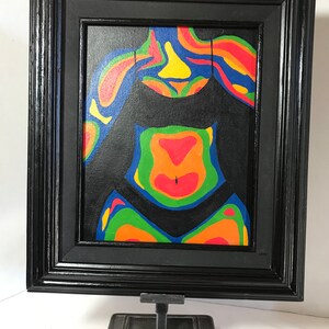 May include: A framed painting of a colorful abstract figure in a black swimsuit. The figure is painted in shades of red, orange, yellow, green, and blue. The painting is framed in a black frame.