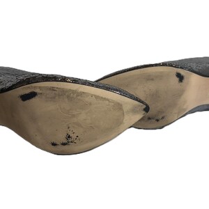 May include: A pair of silver sequined high-heeled shoes. The shoes have a pointed toe and a stiletto heel. The soles are beige with some wear. The shoes are angled, showing the underside and side profile.