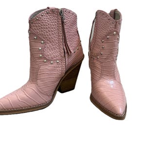 Peut inclure: Une paire de bottes de cow-boy roses avec un bout pointu et un motif texturé en forme de crocodile. Les bottes ont une fermeture éclair latérale, des clous argentés et un talon en bois. Chaussures de mode.