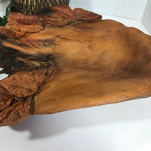 May include: A large, hand-carved wooden bowl with a natural, organic shape. The bowl is made of light brown wood and features carved leaf details on one side. The bowl is approximately 20 inches long and 12 inches wide.