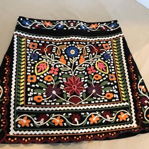 Puede incluir: Una minifalda negra con coloridos patrones florales bordados. La falda tiene un dobladillo festoneado y una cintura negra.