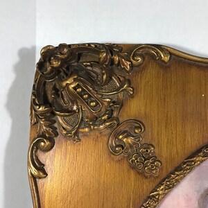 May include: A gold-toned ornate picture frame with a detailed floral design. The frame is made of wood and has a slightly curved shape.