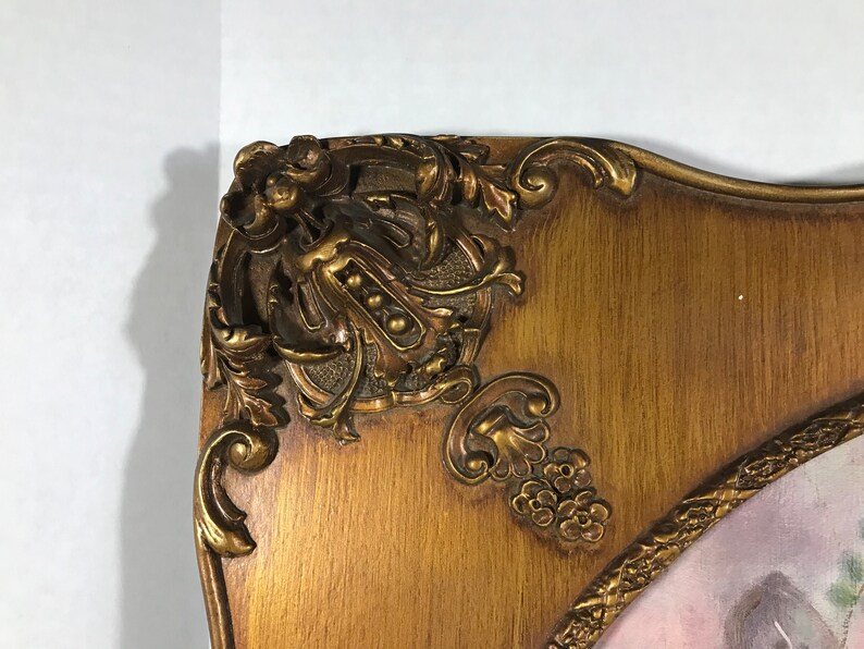 May include: A gold-toned ornate picture frame with a detailed floral design. The frame is made of wood and has a slightly curved shape.