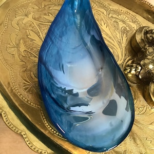 May include: A blue glass bowl shaped like a seashell, sitting on a gold tray with an ornate design.