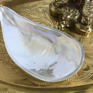 May include: A white iridescent glass dish shaped like a seashell. The dish is sitting on a gold tray with an ornate design.