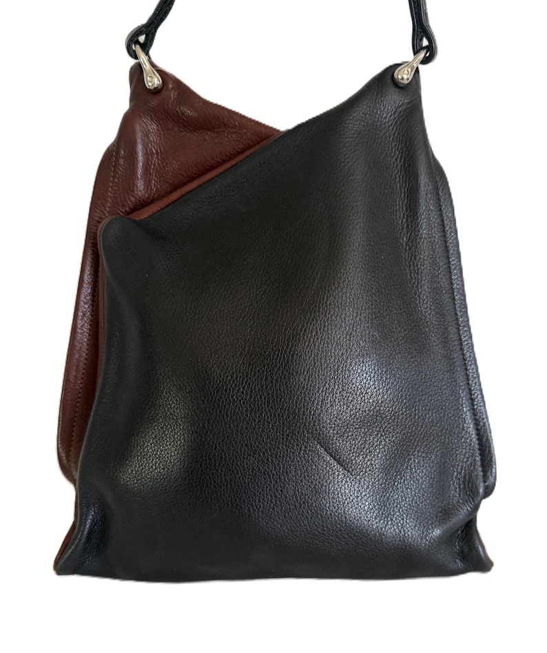 Puede incluir: Un bolso de hombro de cuero negro y marr&oacute;n con una correa negra. El bolso est&aacute; hecho de cuero suave y tiene un dise&ntilde;o simple y minimalista. El bolso es de tama&ntilde;o mediano y parece estar vac&iacute;o.