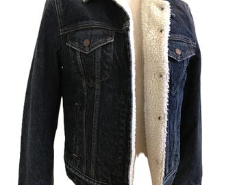 May include: Dark blue denim jacket with a white sherpa lining. The jacket has two chest pockets, two side pockets, and gold star embellishments on the collar. The jacket is displayed on a mannequin.
