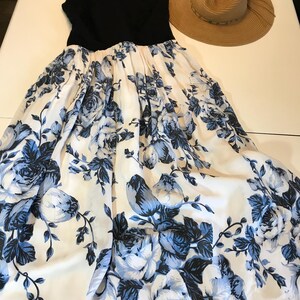 May include: A black sleeveless dress with a full skirt, featuring a white background and blue floral print. A straw sun hat with a wide brim is next to the dress. The dress has a beaded neckline.