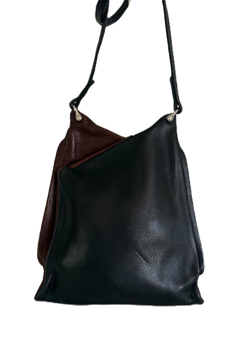 Puede incluir: Un bolso de hombro de cuero negro con una correa larga y delgada. El bolso tiene un dise&ntilde;o suave y holgado. Una segunda bolsa, de color burdeos oscuro, es parcialmente visible detr&aacute;s de la bolsa negra. Las bolsas est&aacute;n hechas de cuero texturizado.